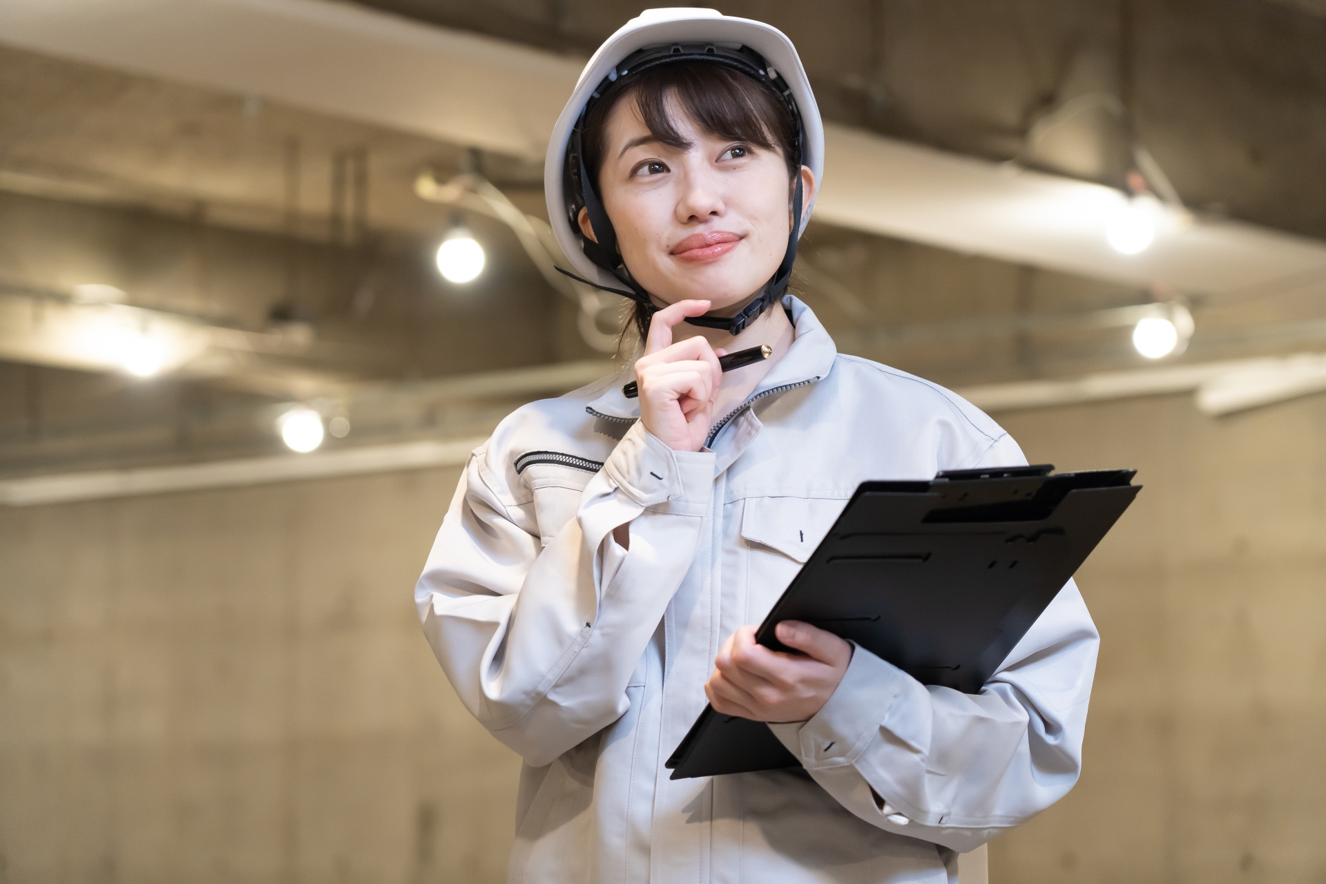 ヘルメットをかぶり、作業着姿でクリップボードを持つ女性技術者